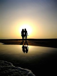 Silhouette people on beach against clear sky during sunset