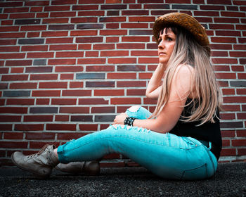 Young woman sitting against brick wall