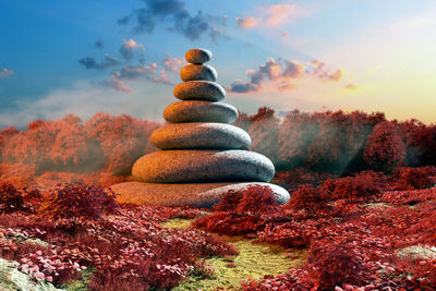 Stack of stones on rock against sky during sunset