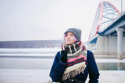 Young woman smoking while standing by bridge against sky during winter