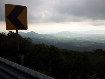 Road sign by trees against sky