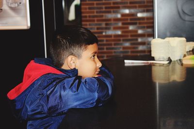 Cute boy looking away while sitting by table at home