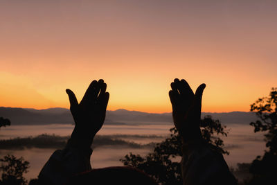 Cropped silhouette hands gesturing against orange sky during sunset