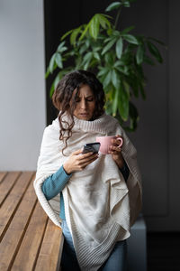 Young unhealthy woman suffering from cold or flu writing sick day email message via smartphone