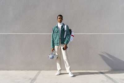 Young man with with radio and bag standing against gray wall