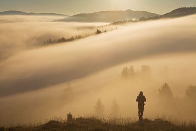 Rear view of silhouette man standing on land against sky during foggy weather