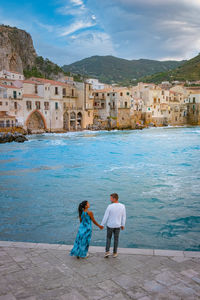 Rear view of women walking on shore against cityscape