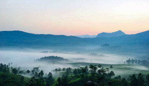 Scenic view of mountains and mist against sky during sunrise