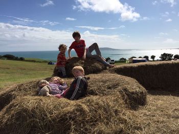 Siblings enjoying on hay at farm against sky