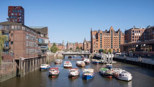 Sailboats moored on canal by buildings against clear sky