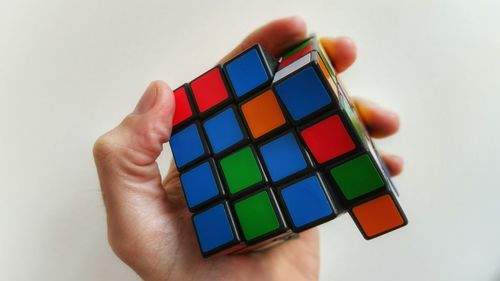 Cropped hand of person holding puzzle cube against wall