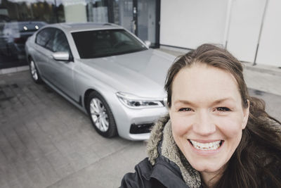 Close-up portrait of smiling woman standing against car outside showroom