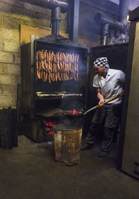 Manual worker inserting coal in smokehouse while preparing sausages at food factory