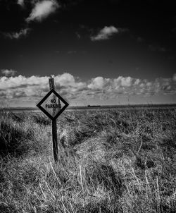 Road sign on field against sky