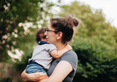 Side view of mother holding son standing outdoors