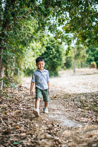 Cute boy looking down and walking against trees