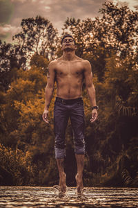 Full length of shirtless man standing against trees