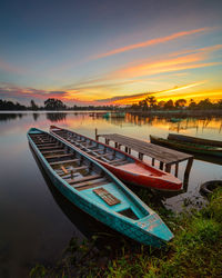 Boats moored in lake against sky during sunset