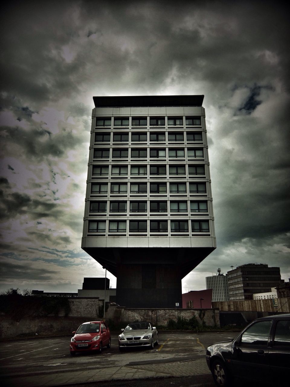 car, transportation, land vehicle, building exterior, architecture, mode of transport, sky, built structure, cloud - sky, street, cloudy, road, city, cloud, building, low angle view, stationary, outdoors, day, no people