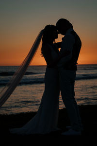 Couple standing on beach against sky during sunset