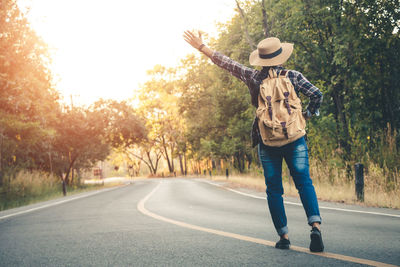 Rear view full length of woman hitchhiking on road