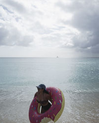 Woman with inflatable ring by sea against sky
