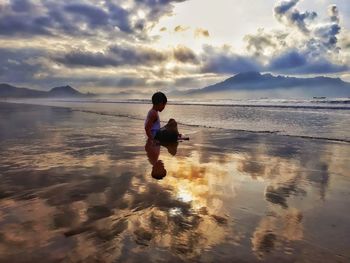 Full length of boy on beach against sky during sunset