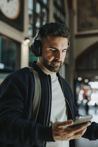 Man wearing bluetooth headphones holding smart phone at station