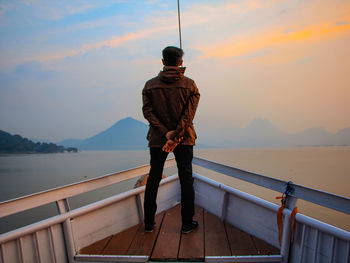 Man standing on railing by mountain against sky