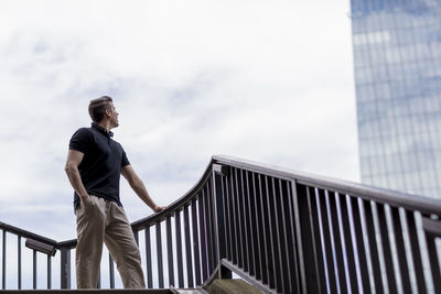 Low angle view of man looking at building against sky in city