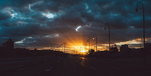 Cars on road against dramatic sky during sunset