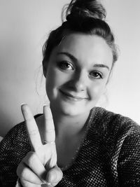 Portrait of smiling young woman showing peace sign against wall