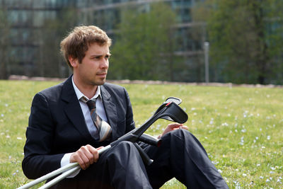 Businessman sits in a park in the city with crutches after knee injury