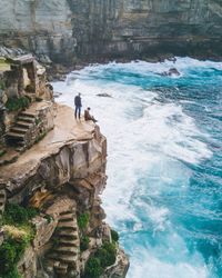 Man standing on cliff by sea against sky