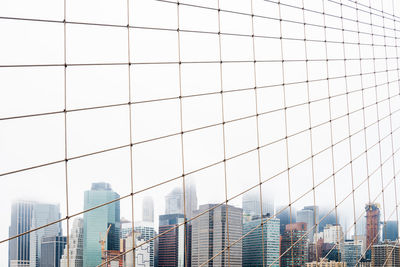 Low angle view of buildings seen through fence against sky