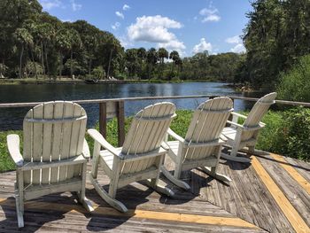 Wooden rolling chairs by lake against trees