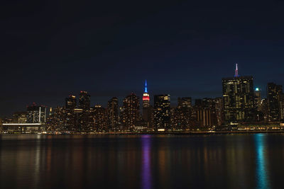Illuminated buildings by river against sky at night