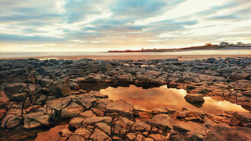 Rocks at beach against cloudy sky during sunset