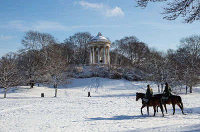 People riding a horse on snow covered landscape against sky