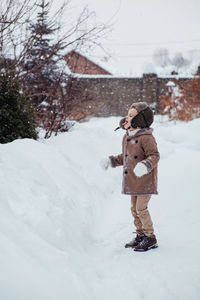 A boy in a winter hat and coat rejoices in the snow. the child catches snowflakes with his tongue. 