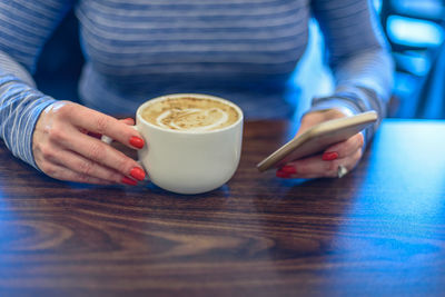 Midsection of woman holding coffee cup on table