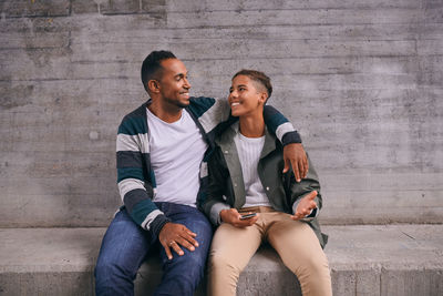 Cheerful father and son looking each other face to face while sitting against wall