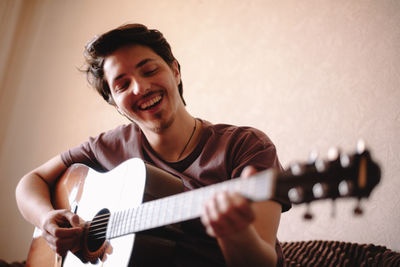 Cheerful young man playing guitar at home