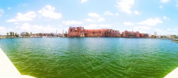 Sea by buildings in city against sky