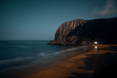 Scenic view of beach and rock against sky at night