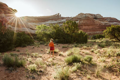 Woman walks away as sun sets over the canyon walls in a desert oasis