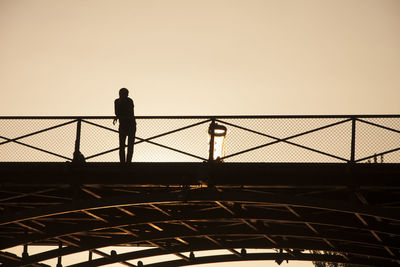 Low angle view of silhouette man leaning on pont des arts railing during sunset