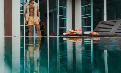 Woman standing by swimming pool against window