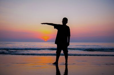 Silhouette man standing on beach against sky during sunset