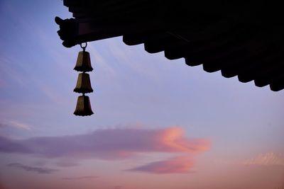 Low angle view of bells hanging from roof against sky during sunset